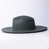 The SEXY BRIM HAT is displayed against a white background, showcasing its dark green hue and smooth texture. The hat features a wide brim and a slightly rounded crown, giving it an effortlessly sleek and stylish look.