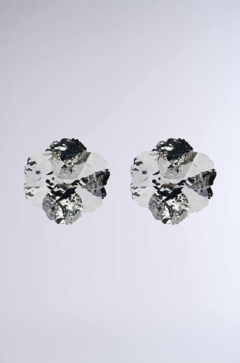The image showcases two PICTURE PERFECT EARRING clusters, akin to abstract floral designs, crafted from shiny, metallic faux silver minerals. Set against a plain light gray background, these clusters gleam with reflective surfaces and intricate angles, reminiscent of statement earrings with geometric flair.