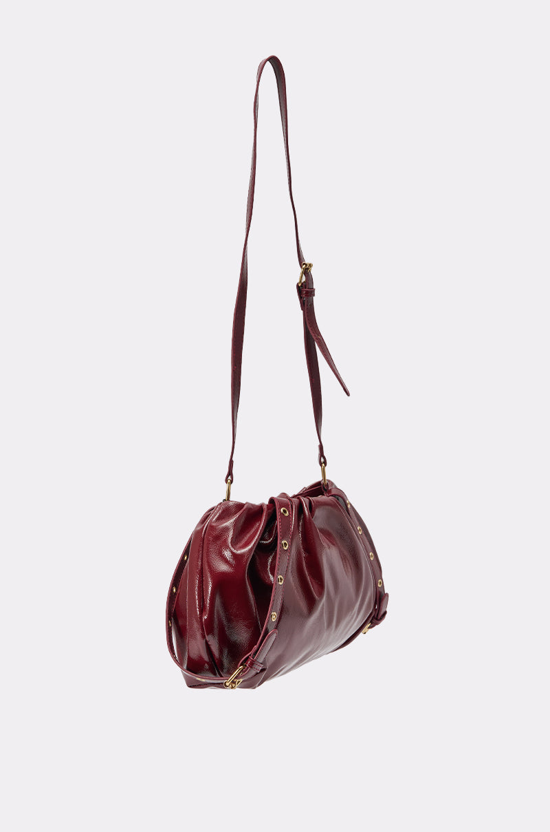 THEE BURGUNDY Y2K RUCHED PURSE features red faux patent leather, gold stud accents, gathered detailing, and an adjustable crossbody strap, shown against a plain light background. 4