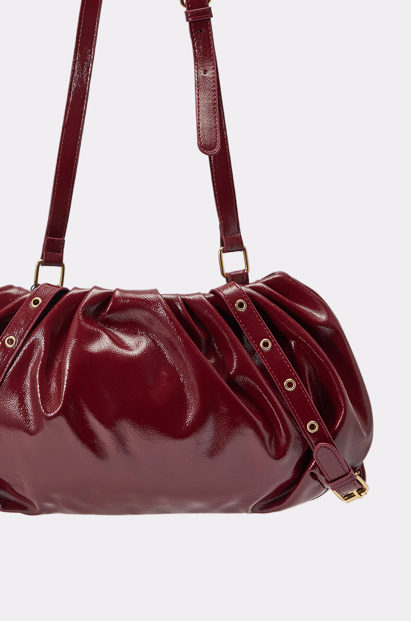 THEE BURGUNDY Y2K RUCHED PURSE—a glossy dark red faux patent leather shoulder bag with gold-tone buckles and an adjustable crossbody strap—displayed against a plain light background. 5