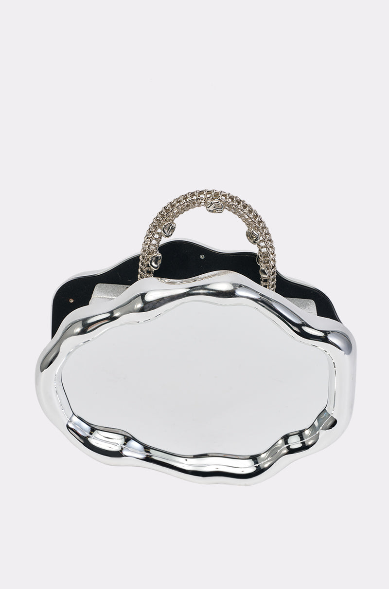 Introducing the MIRROR MIRROR ON THE WALL BAG—a sculptural handbag featuring a shiny, wavy-edged metallic silver front and a braided metallic handle, beautifully displayed against a plain white background.