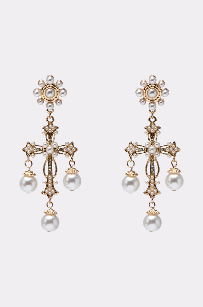 The CROSS IT OUT EARRING is a pair of gold-tone cross earrings with ornate floral tops, pearl accents, and three dangling white pearls on each. Displayed against a plain light gray background. 1