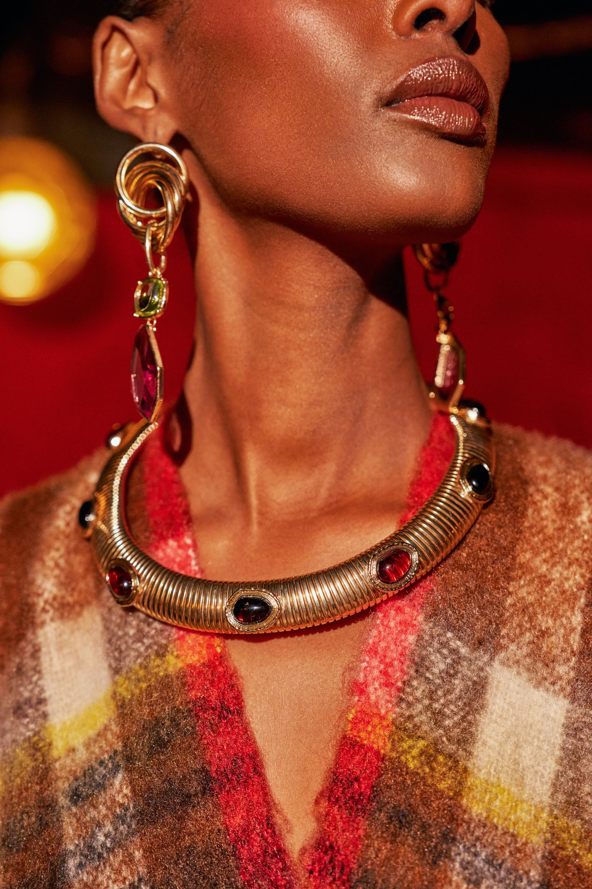 A person wears a sculptural, wide ridged gold SERPENT SUN NECKLACE set with cabochon stones and matching long drop earrings.