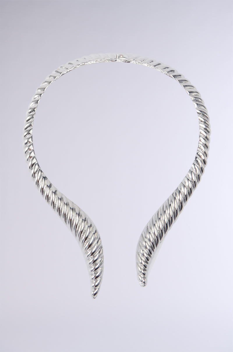 The TOO TUFF NECKLACE is presented against a plain background, showcasing its silver twisted torc design with open ends from the AKIRA Label. This statement jewelry piece boasts intricate spirals along its length, offering a sophisticated and elegant look that emphasizes its metallic silver sheen.