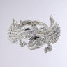 The REPTILE MANIA CUFF is an ornate faux silver metal bracelet that showcases the intricate designs of two rhinestone-embellished reptiles entwined together. Detailed with numerous small, sparkling crystals, the alligators face each other and form a circular shape against a plain light gray background.