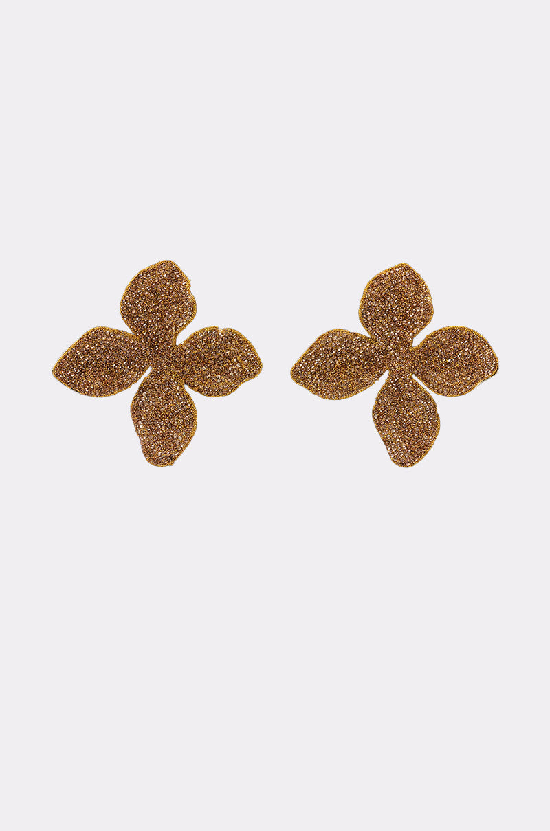 The GOLDEN GLAM EARRING is a pair of gold, glittery, four-petal flower statement earrings shown on a plain white background. 1