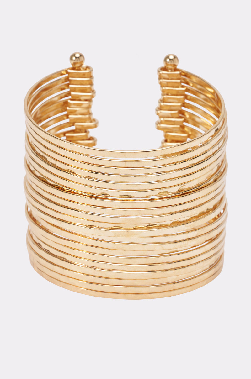 The GOLD HAMMERED CUFF showcases multiple thin, stacked bands with a wide hammered gold design and an open back, displayed against a light background—an effortlessly chic statement piece for any occasion.