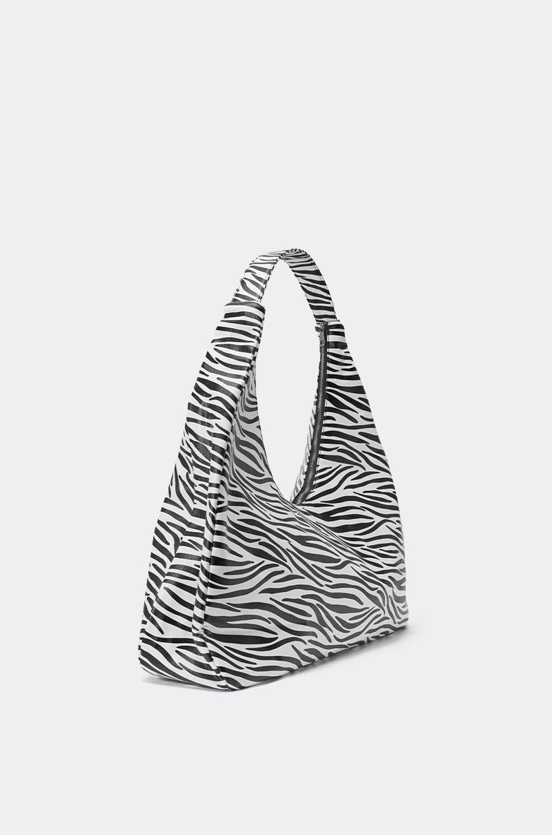 The IN THE WILD OVERSIZED TOTE is a black and white zebra print bag with a curved, modern design made from faux leather, shown on a plain light gray background. 2