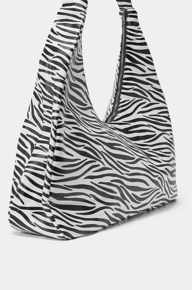The IN THE WILD OVERSIZED TOTE is a triangular zebra-print bag with black and white stripes, made from faux leather and finished with a top zipper closure. 3