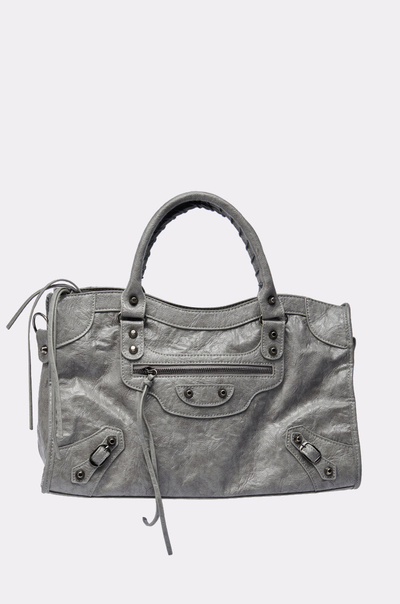The ROSIE OVERSIZED PU TOTE is a gray faux leather handbag with two handles, a front zipper pocket, decorative studs, and long zipper pull tassels, shown against a plain white background.