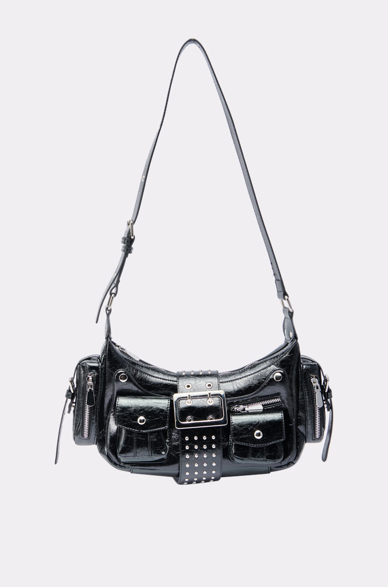 Streetwear-inspired, THE TIDUS PU PURSE features glossy faux patent leather, a long adjustable strap, front buckle detail, silver studs, two snap-closure pockets, and side zipper pockets on a light background. 3