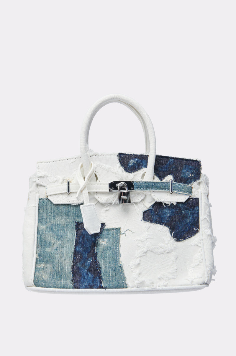 The IT IS WHAT IT IS PURSE is a white handbag with dual handles, featuring a structured shape, blue and white patchwork distressed denim, plus silver-tone buckle and strap accents. 1