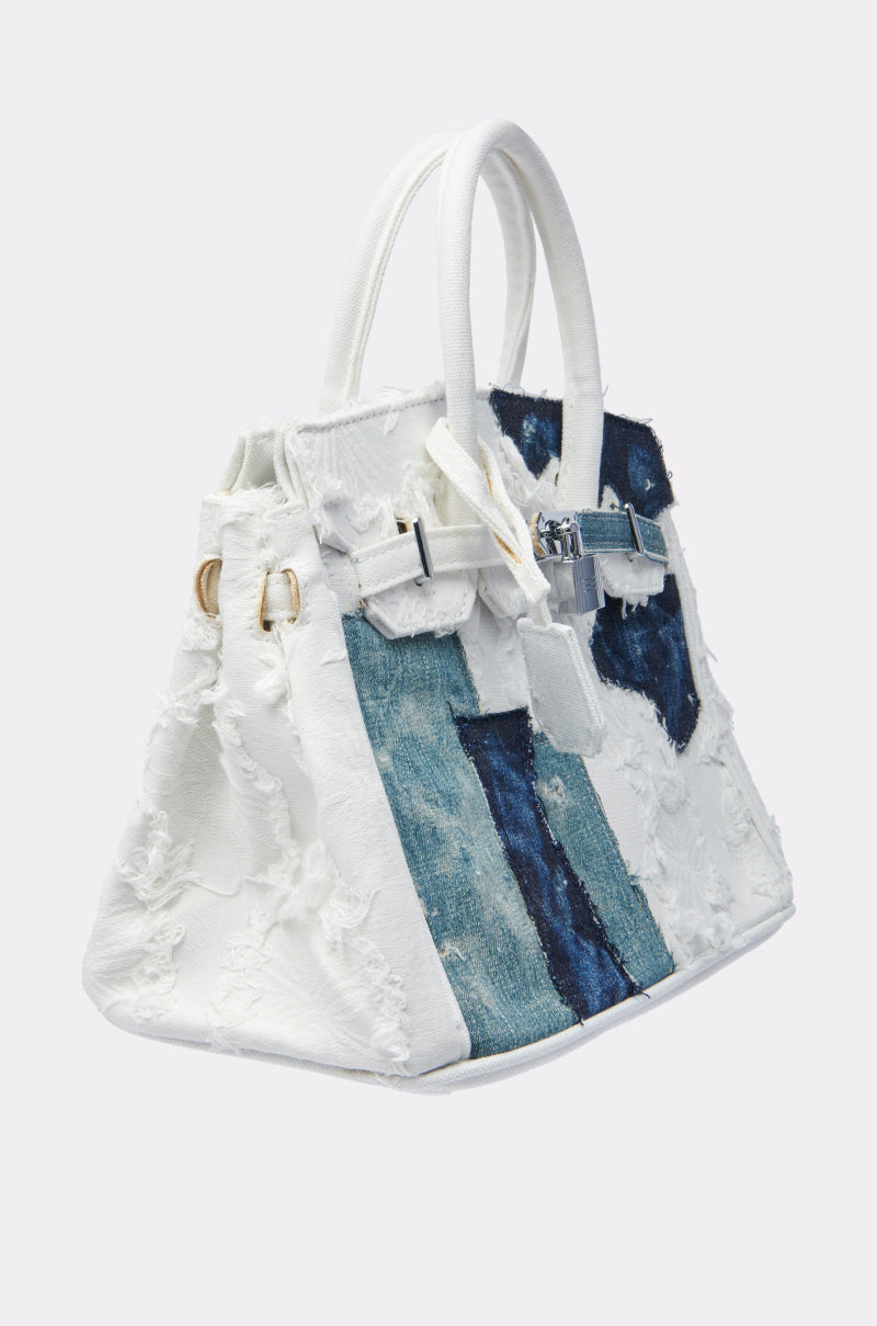 The IT IS WHAT IT IS PURSE is a stylish handbag with a structured silhouette, white handles, distressed white and blue denim patchwork, and a silver front clasp. 2