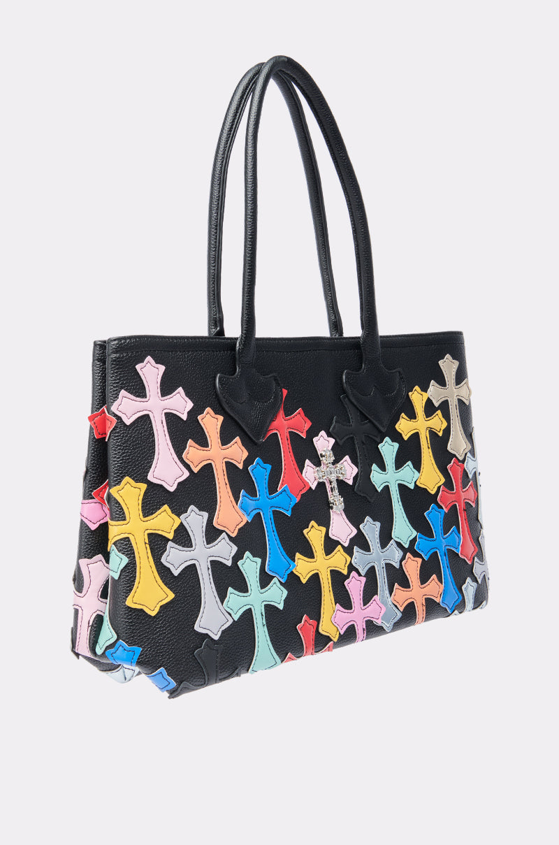The PERSONAL PROBLEM CROSS TOTE is a black handbag with two handles, featuring colorful leather cross-shaped patches in pink, yellow, blue, red, and purple on the front and sides.