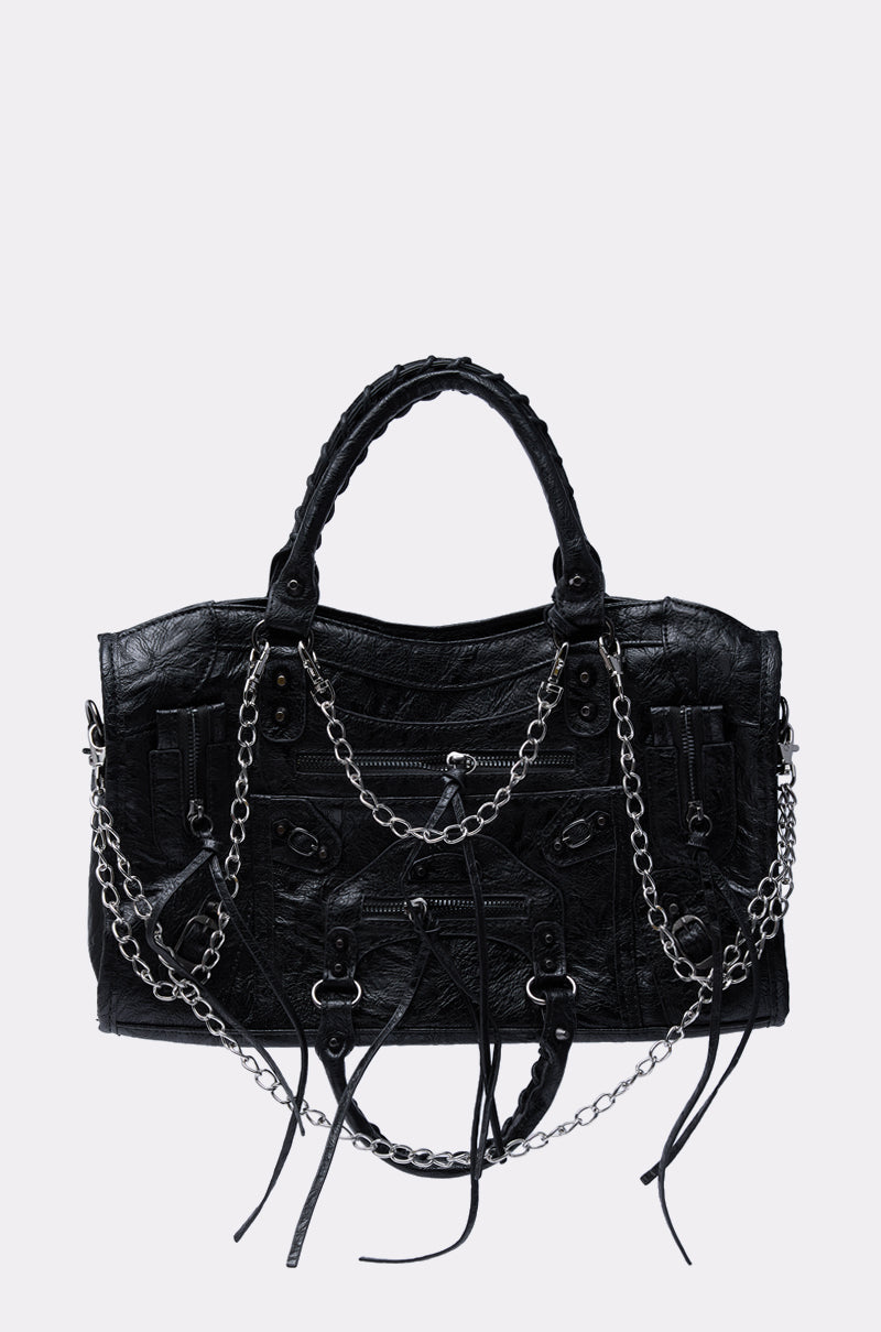 The YOUR LOSS PURSE is an edgy black faux leather handbag with silver chain accents, zipper details, two handles, and long tassels hanging from the zippers, shown against a plain light background.