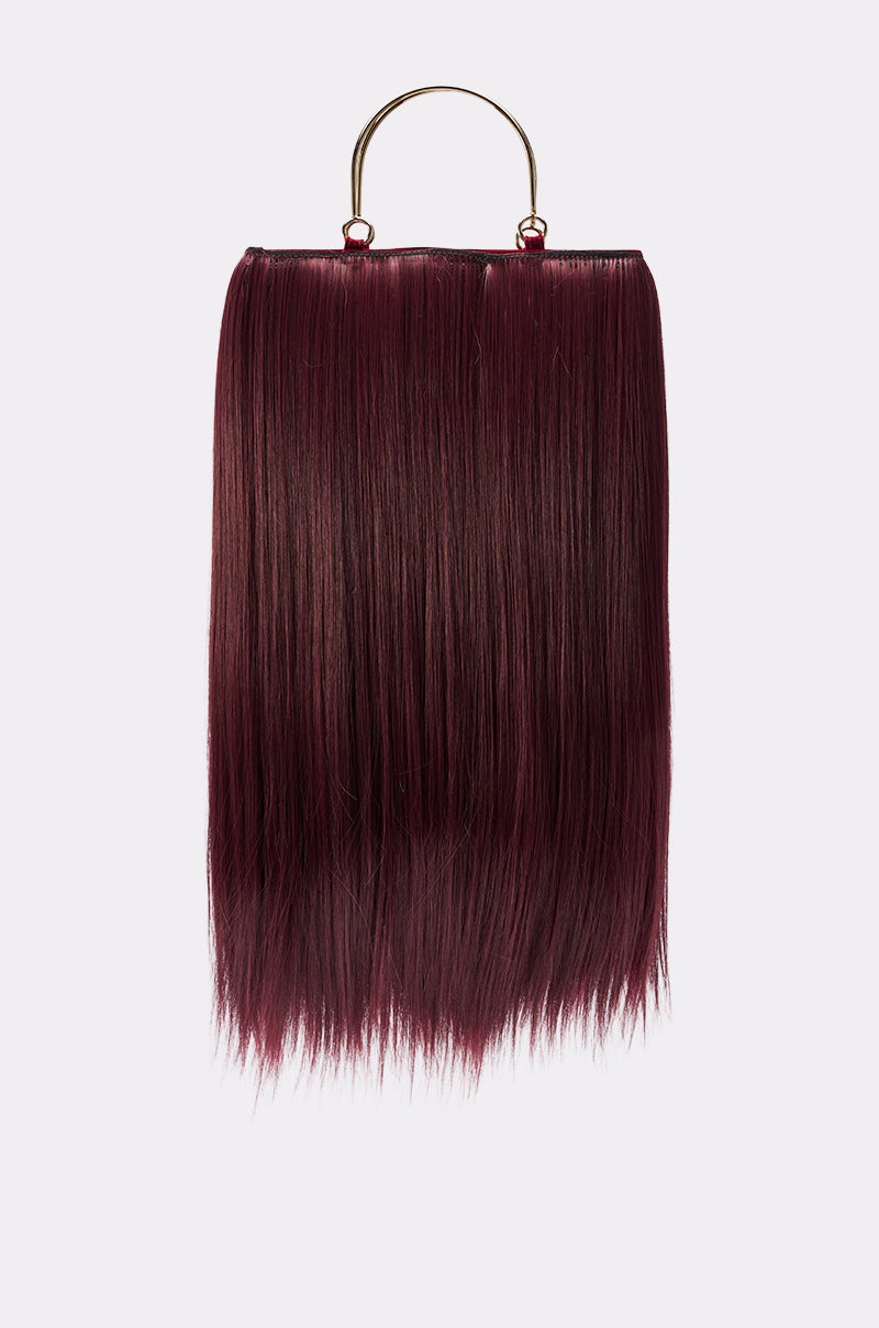 The MY HAIR PURSE features a rectangular sheet of long, straight, dark burgundy synthetic hair forming its body, suspended from a metallic gold handle and set against a plain light gray background.