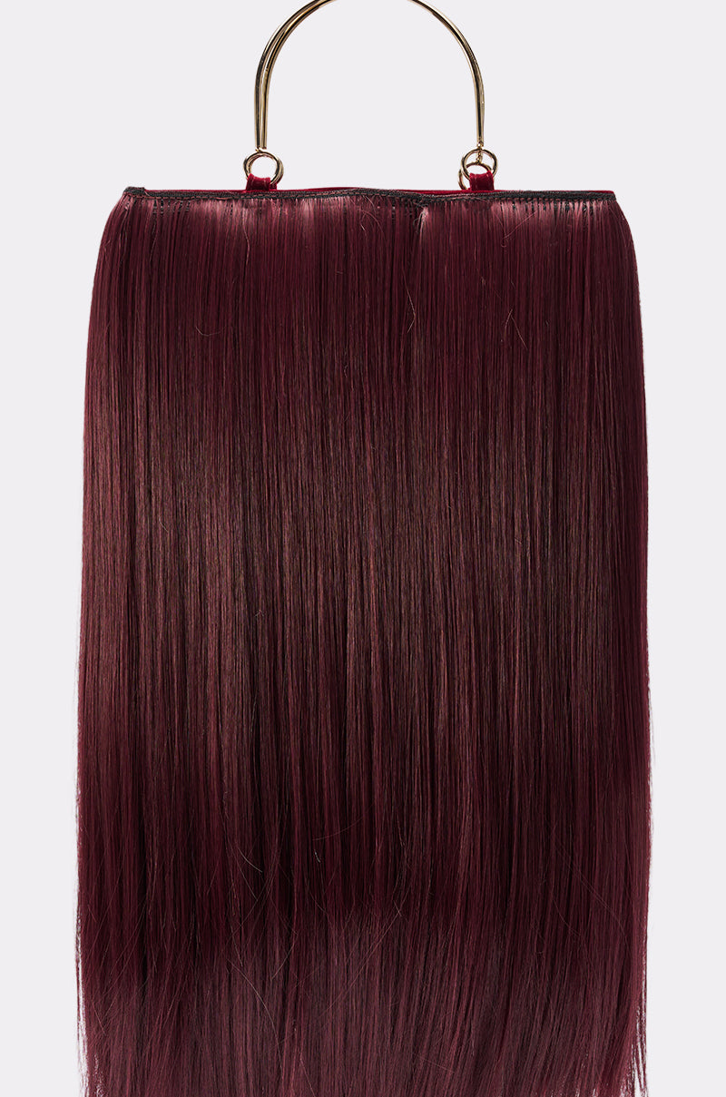 The MY HAIR PURSE is a rectangular burgundy bag designed to resemble long, straight hair, featuring a striking gold-tone top handle.