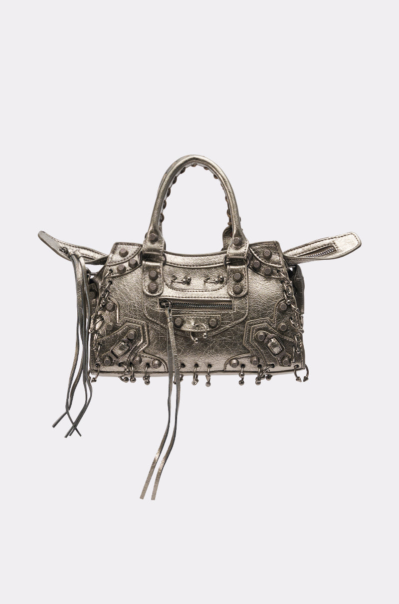 The GRUNGE PIERCED PURSE is a metallic silver bag with decorative studs, buckles, zipper accents, two short handles, and long tassels—combining edgy grunge style with standout details. 2