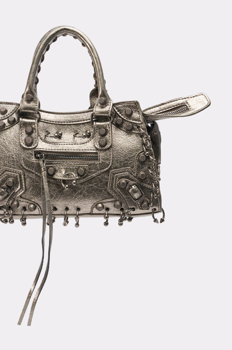 The GRUNGE PIERCED PURSE is a metallic silver bag with decorative studs, zipper accents, textured surface, two handles, pierced and visible hardware, tassel details, and a bold edgy style set against a plain light background.