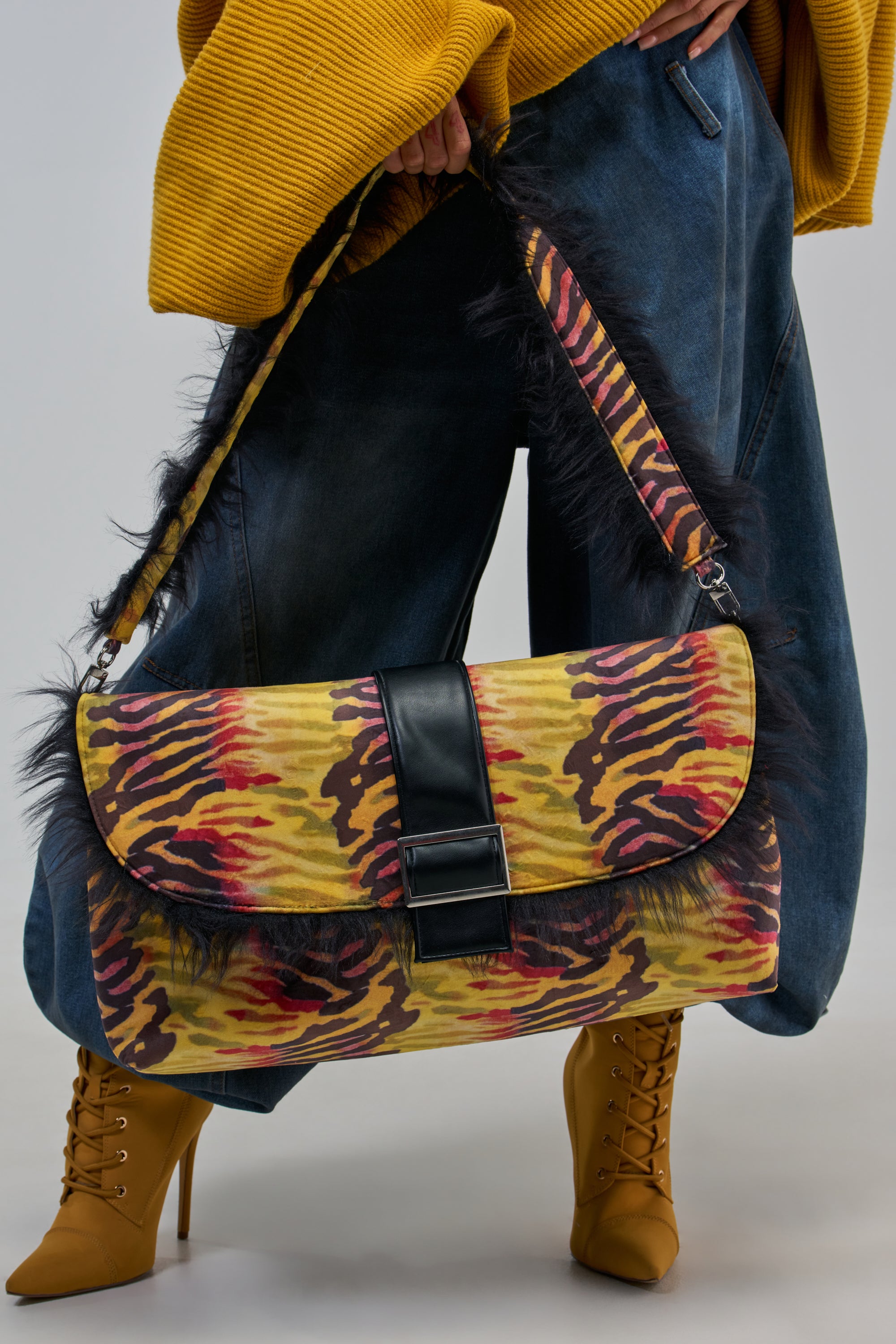 Wearing wide-leg jeans and tan boots, this person carries the SERIOUSLY TIGER BAG—a large tiger print shoulder bag with black fur accents—while a yellow oversized sweater adds to the bold look.