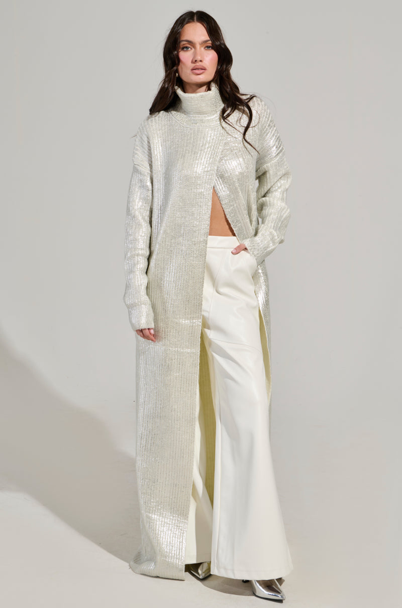 A woman is wearing the WORTHY OF LOVE Long Sleeve Metallic Sweater in Silver, styled over white wide-leg pants and paired with metallic shoes. The sweater boasts a high collar and an open front. She has long brown hair and is posing against a plain light background.