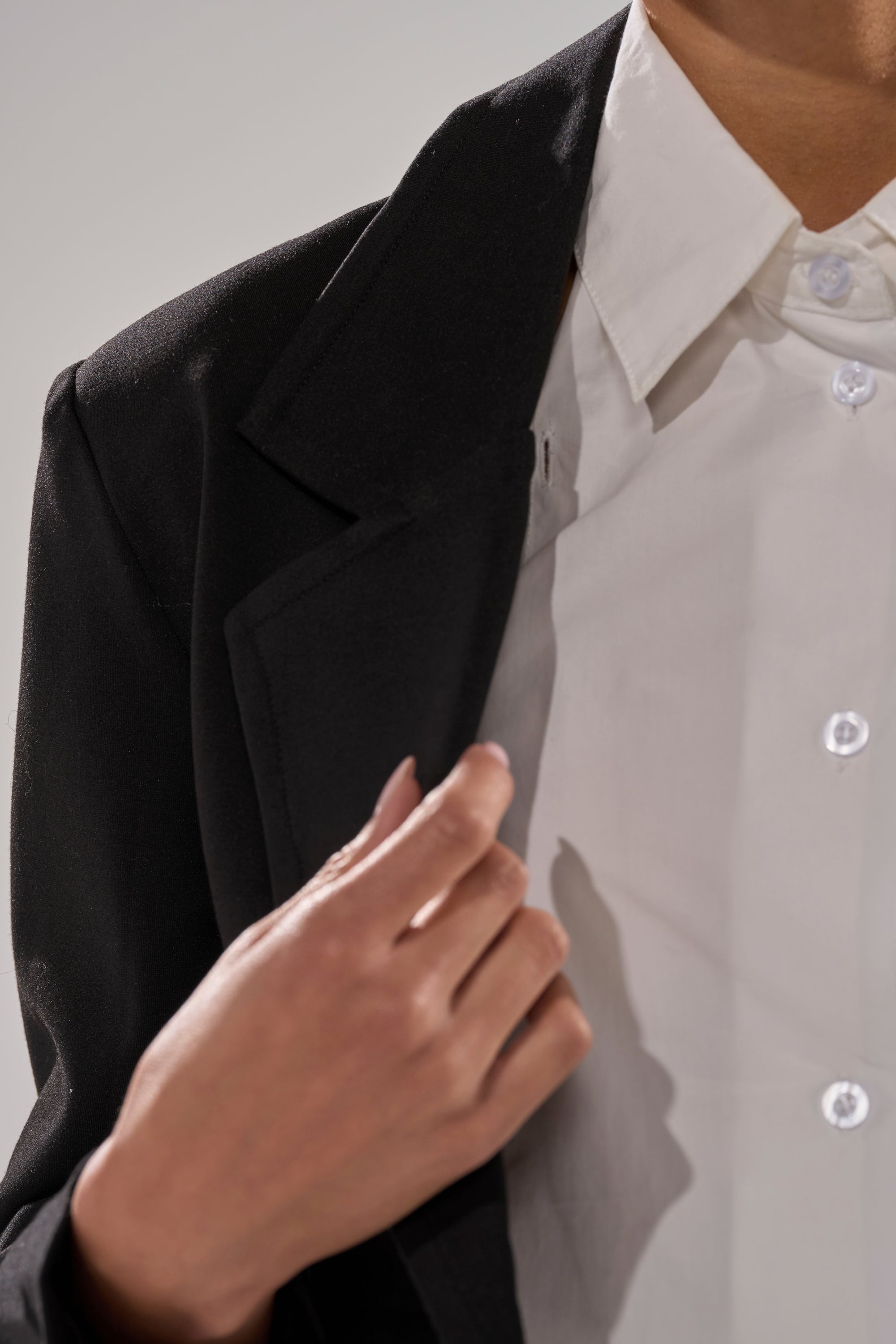 A person adjusts the collar of a white button-up shirt while wearing the BLACK TIE FORMAL TOP, with only their hand and part of their torso visible.