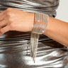 A close-up of a person in a shimmering silver dress and the Waterfall Love Cuff in Silver, featuring a wide band with cascading rhinestone fringe. The dress and cuff reflect light, creating a luxurious and elegant appearance.