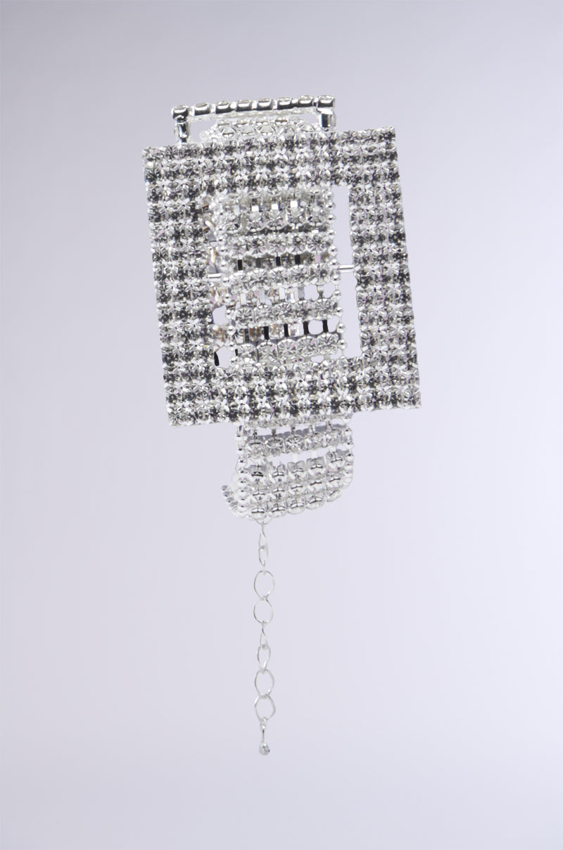 Introducing the BUCKLE UP BRACELET: a silver geometric accessory adorned with cascading rows of sparkling crystals, reminiscent of rhinestone detailing against a plain gray background. The bracelet elegantly features design elements that evoke the look of a sophisticated faux buckle pendant.