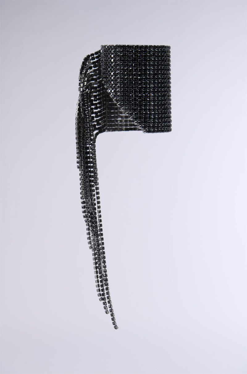 The MIDNIGHT WATERFALL CUFF is a sleek and contemporary black bracelet, meticulously crafted from small, glossy square tiles. This exquisite piece is adorned with pave rhinestone embellishments and boasts a distinctive cascading design, complemented by long chain link fringe trim that flows elegantly from the main cuff, creating a stunning and dynamic look against any plain backdrop.