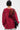 A person with short dark hair is seen from behind, wearing an oversized OPEN FOR BUSINESS SWEATSHIRT IN BURGUNDY with rhinestone mesh paneling and torn sections, light-colored pants, and carrying a black shoulder bag.