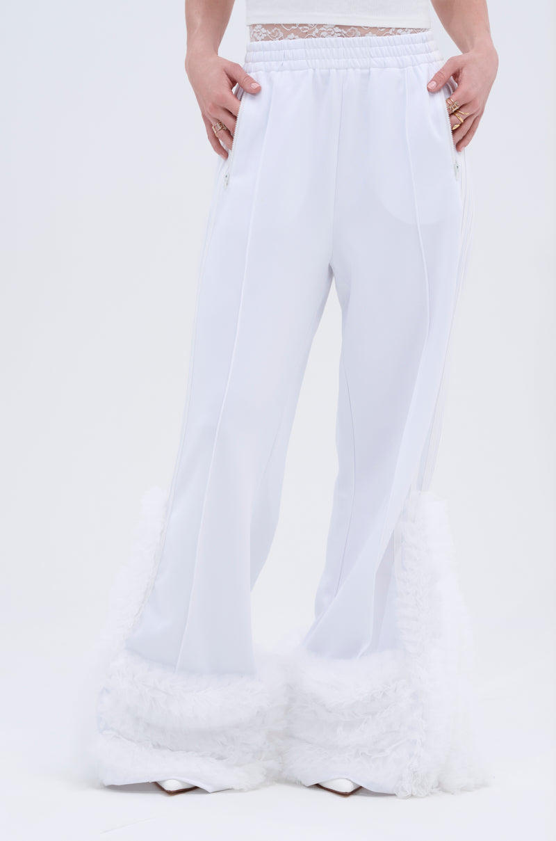 A person wears the MODERN JAM TRACK PANT IN WHITE—high-rise, loose white track pants with fluffy textured hems and a lace waistband—standing against a plain white background. Only the lower torso and legs are visible.