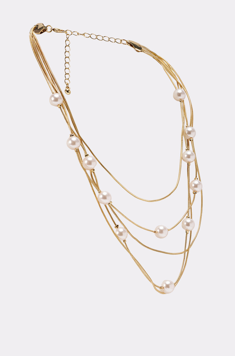 The SHES EXPENSIVE NECKLACE is a gold multi-strand statement piece with evenly spaced white pearls, an adjustable clasp, and extender chain, shown on a plain white background for an elegant look. 3