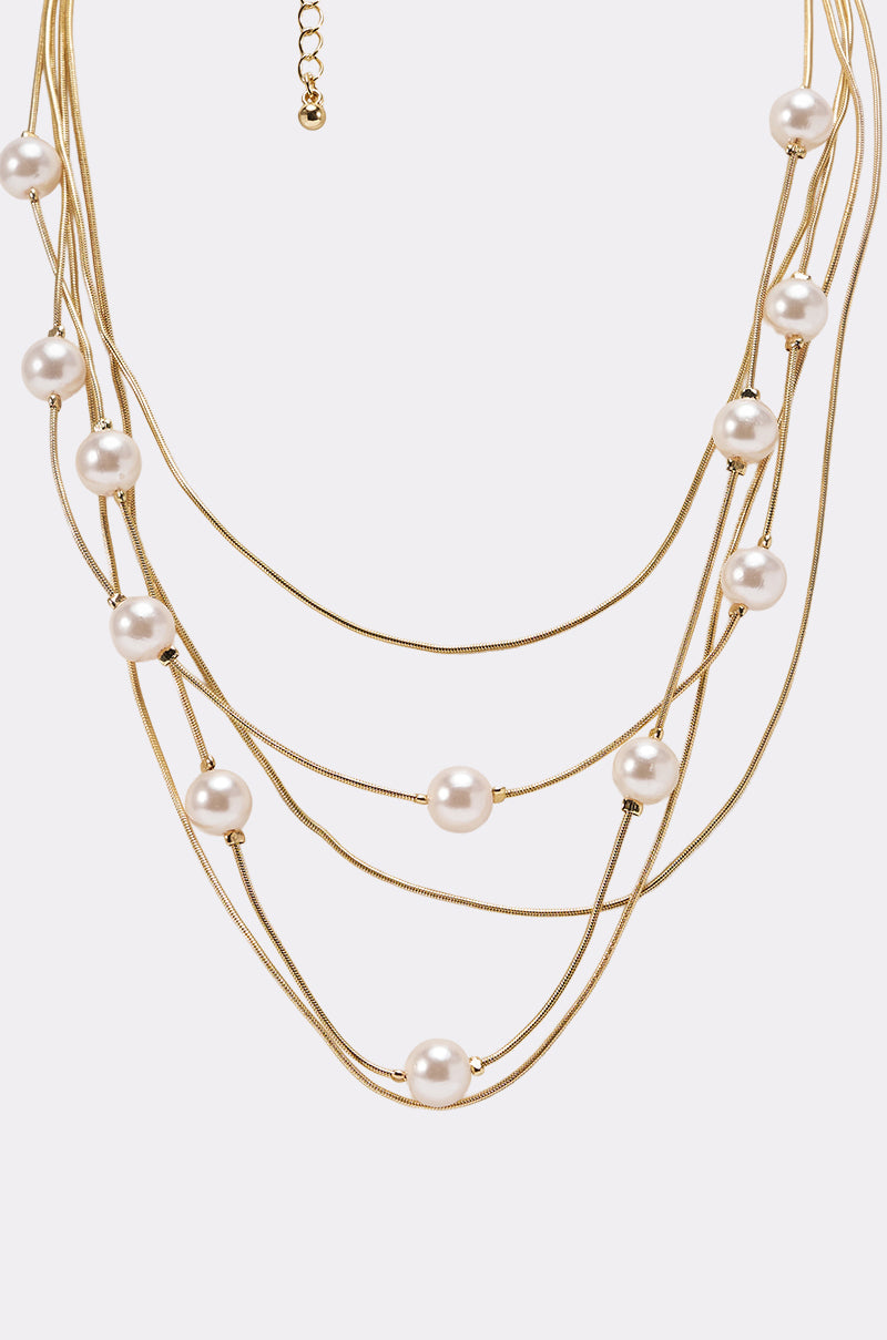The SHES EXPENSIVE NECKLACE is a layered piece with multiple gold chains and evenly spaced round white pearls on each strand, shown against a plain white background. 4