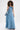 A woman with curly hair wears the STRAPLESS TRENCH MAXI DRESS IN DENIM, oversized sunglasses, a chunky necklace, and carries a matching denim handbag while standing against a plain white background.
