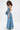 A woman with curly hair wears the STRAPLESS TRENCH MAXI DRESS IN DENIM, paired with dark sunglasses and a matching denim bag, posing confidently against a plain white background.
