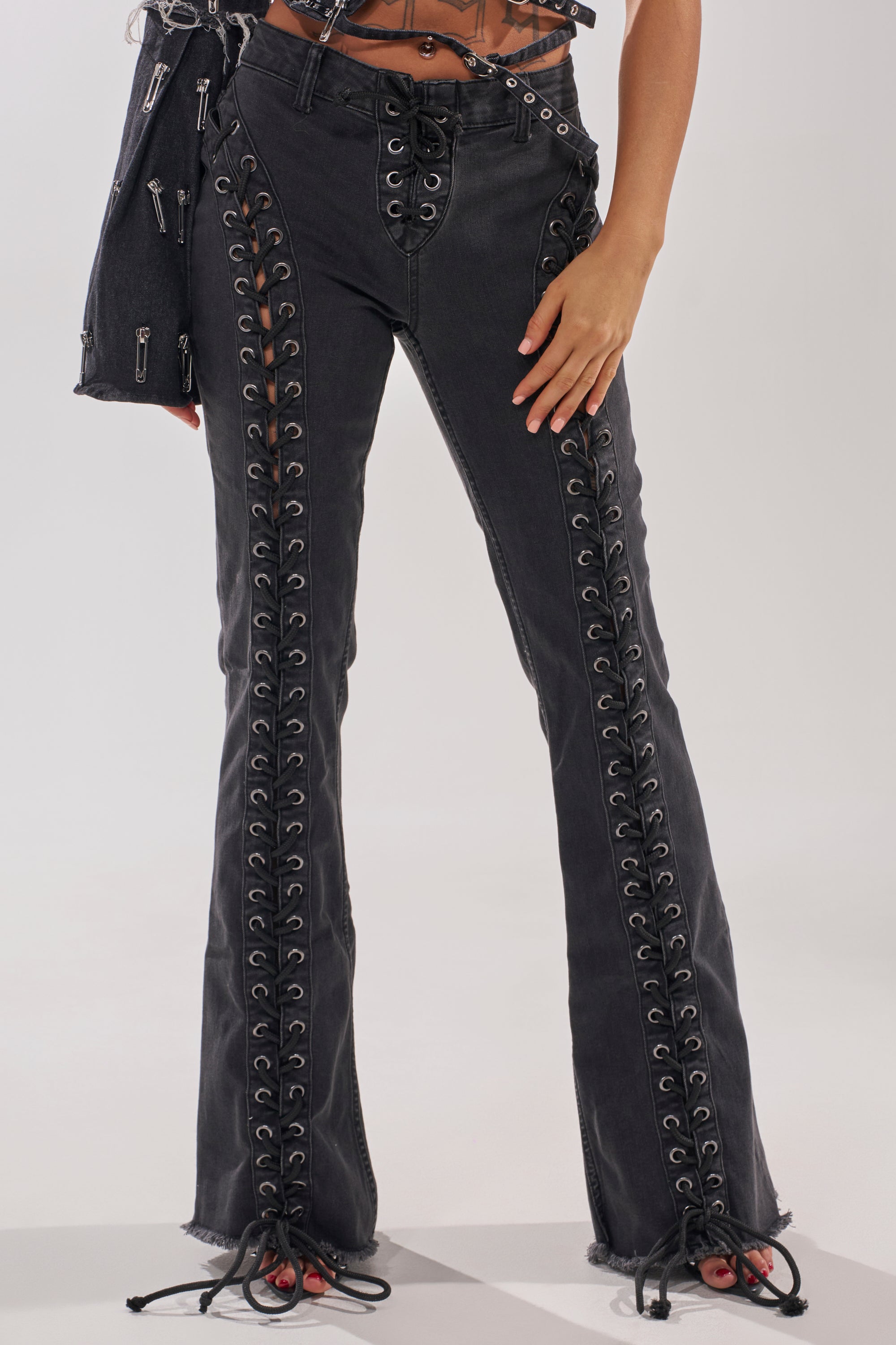 Wearing HOTTY LACE UP FLARE DENIM—high-rise flares with lace-up details and silver eyelets on the front seams and hem—styled with a matching black bag for a chic look. 0