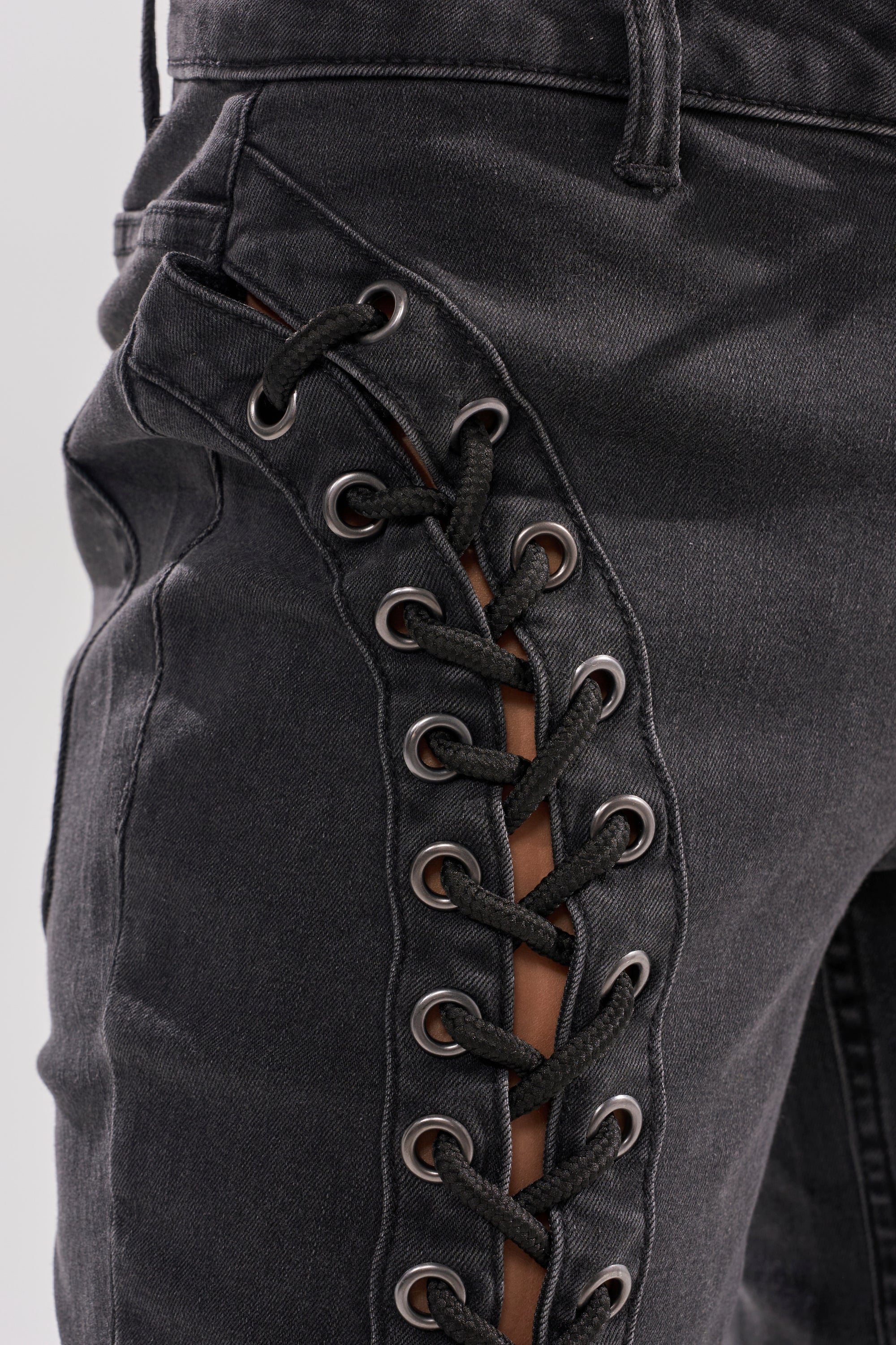 Close-up of the HOTTY LACE UP FLARE DENIM, featuring side lace-up details with black cords threaded through metal eyelets, partially revealing skin underneath. 8