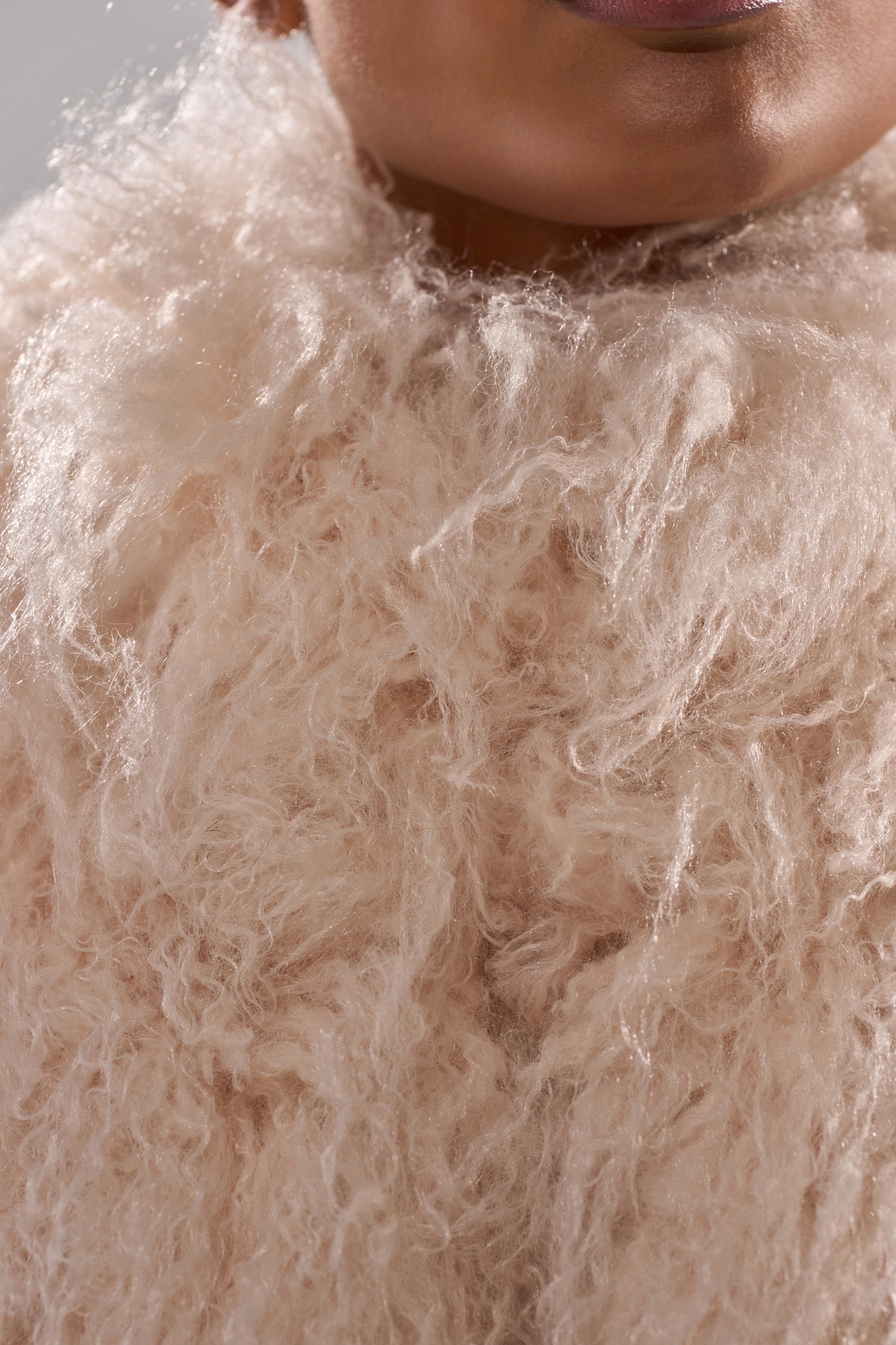 Close-up of a person wearing the COCO Cropped Fur Vest in Beige, featuring a fluffy, textured finish; only the lower half of their face is visible at the top of the image.
