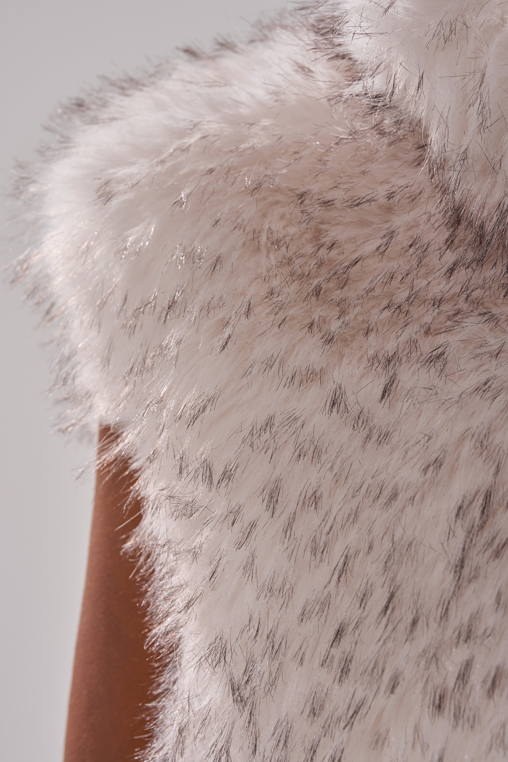 A close-up shows the luxurious texture and speckled detail of the COCO CROPPED FUR VEST IN WHITE MULTI, highlighting its soft faux fur on the shoulder and upper arm.