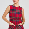 A person models the Best Dressed Plaid Mini Dress in Red, featuring a sleeveless design with gold buttons and hands tucked into its pockets. They accessorize with gold hoop earrings and a chunky chain necklace, while their hair is elegantly pulled back. The tweed-like texture of the dress stands out against the plain white background.