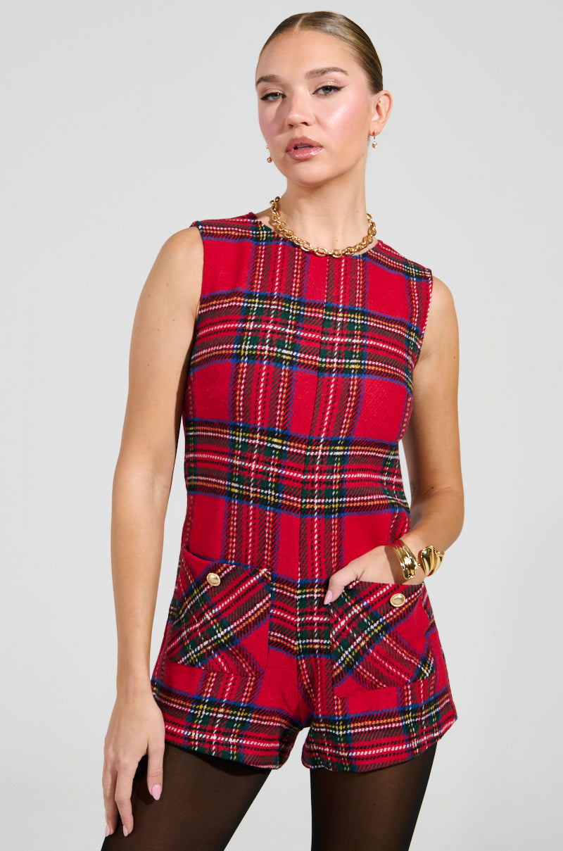With an aura of style, the individual dons the Best Dressed Plaid Mini Dress in Red, showcasing its tweed-like fabric. The sleeveless piece is highlighted by gold buttoned pockets. Paired with black tights, and accessorized with a chunky gold necklace and bracelets, they pose against a plain backdrop.