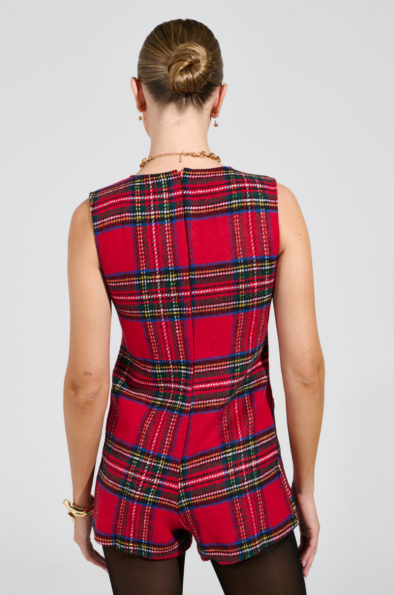 A person with their hair in a bun is wearing the BEST DRESSED PLAID MINI DRESS IN RED, paired with a gold chain necklace and bracelet. The outfit highlights their impeccable style as they face away from the camera against a plain background.