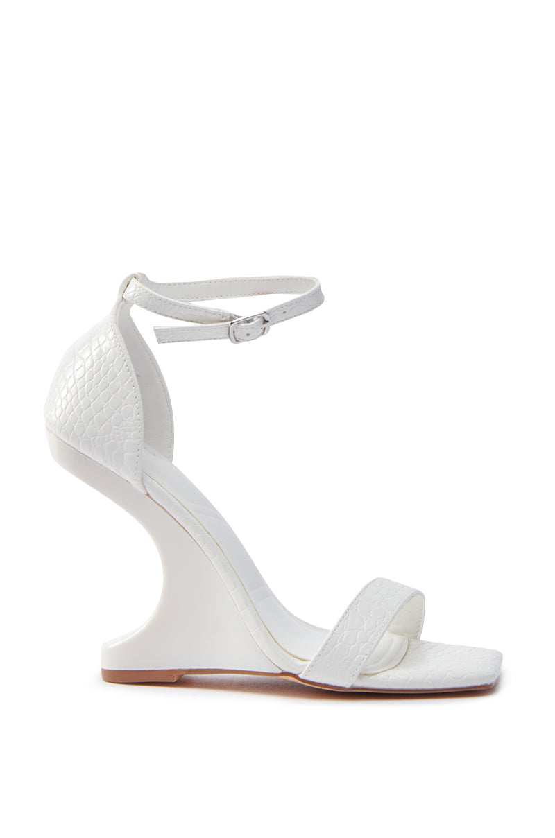 The AKIRA AALTO WHITE SANDAL is a chic white high-heeled sandal with a unique curved wedge and open square toe. It includes an ankle strap with buckle, textured vegan leather details on the heel and toe strap, and a light brown sole.