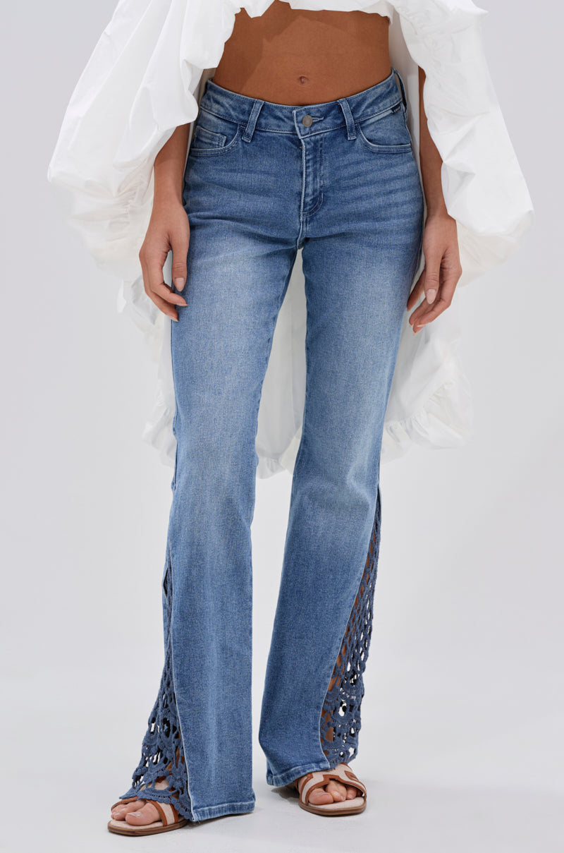 Wearing the SUMMER DAYS RELAXED DENIM WITH EYELET OPENING, a person pairs these blue jeans with a white billowy top and brown sandals, standing against a plain light background. 2