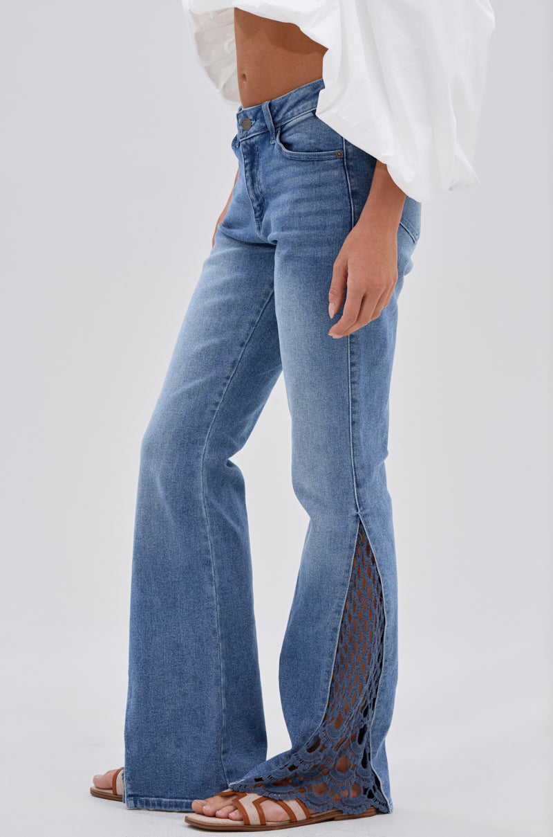 A person wears SUMMER DAYS RELAXED DENIM WITH EYELET OPENING, paired with a white top and brown sandals, standing against a plain light background. 0