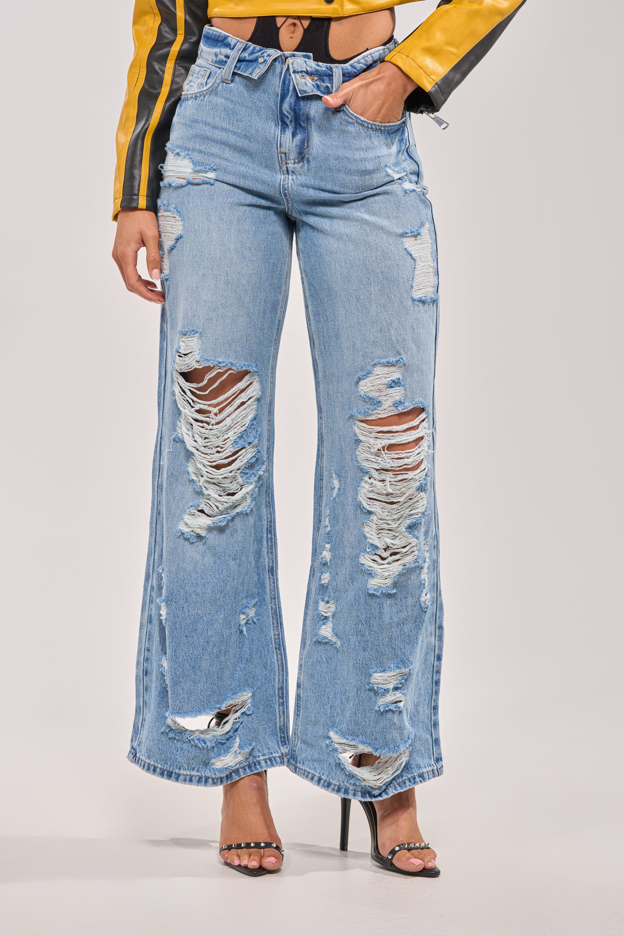 Wearing SOMETHING NEW FOLD OVER WAISTBAND DISTRESSED DENIM jeans featuring a light wash, heavy rips, and folded waistband, styled with a yellow and black jacket and black high-heeled sandals. 1