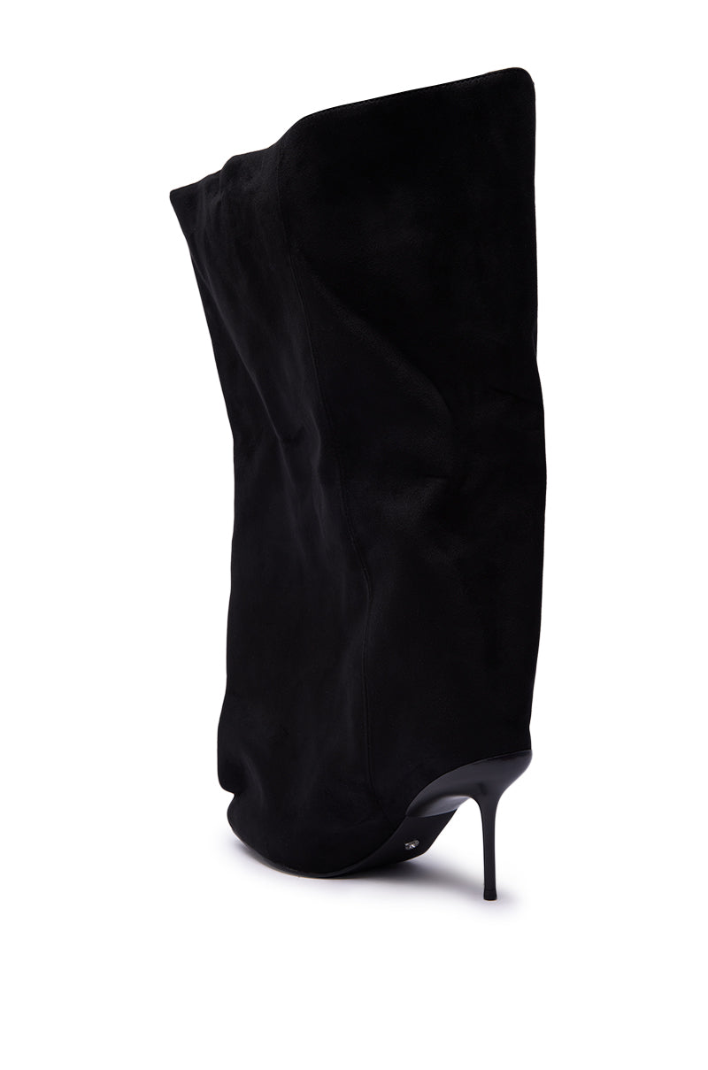 The AZALEA WANG ABAWI BLACK EXTREME BOOT IN SUEDE is a black suede stiletto boot with a pointed toe and a slouchy, oversized shaft. It’s shown from behind at an angle against a white background.
