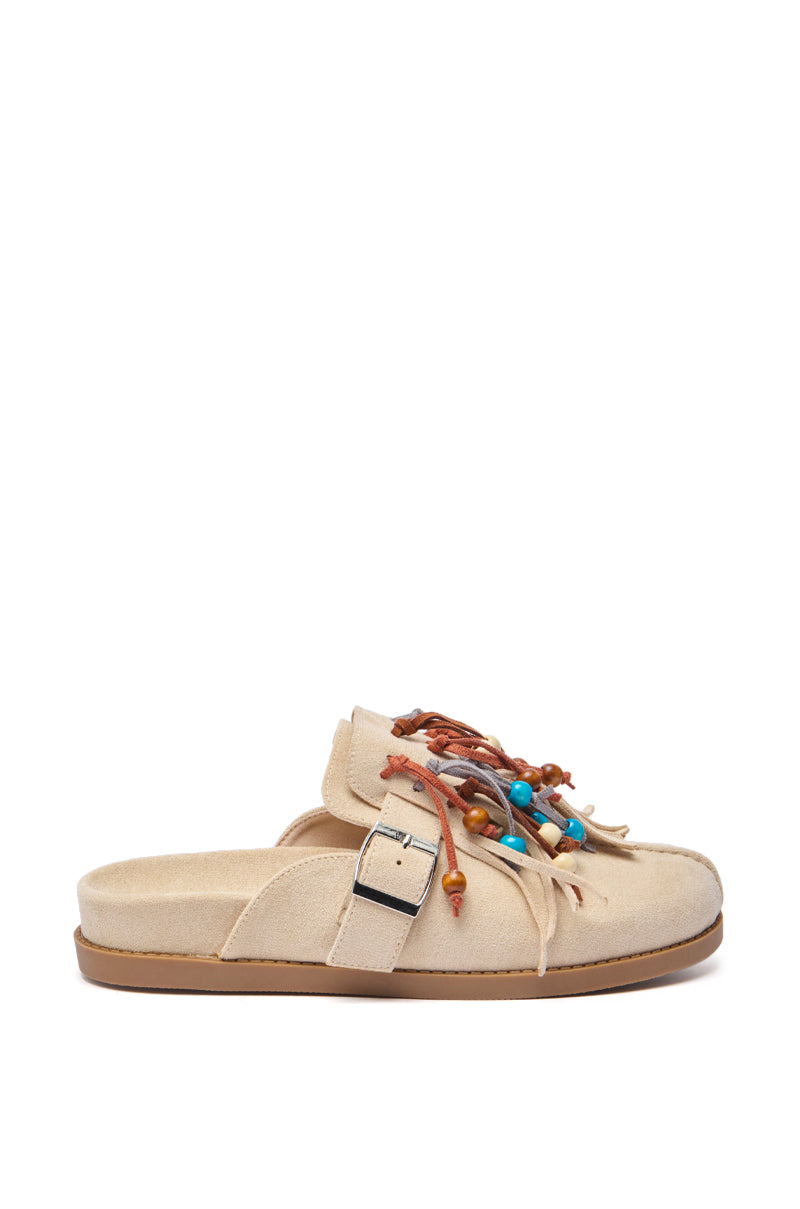 The AZALEA WANG ABEILLE Beige Faux Suede Fringe Clog features an almond toe, flat sole, side buckle, and decorative leather laces with multicolored beads and knots on top.