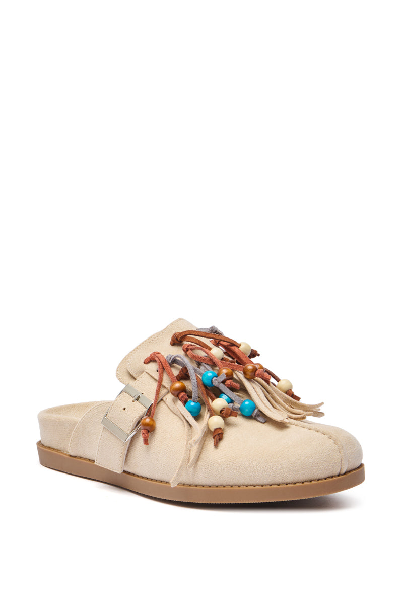 The AZALEA WANG ABEILLE Beige Faux Suede Fringe Clog is a beige slip-on with a flat sole, silver buckle, leather tassels, and blue, brown, and cream beads—ideal for boho shoe lovers.