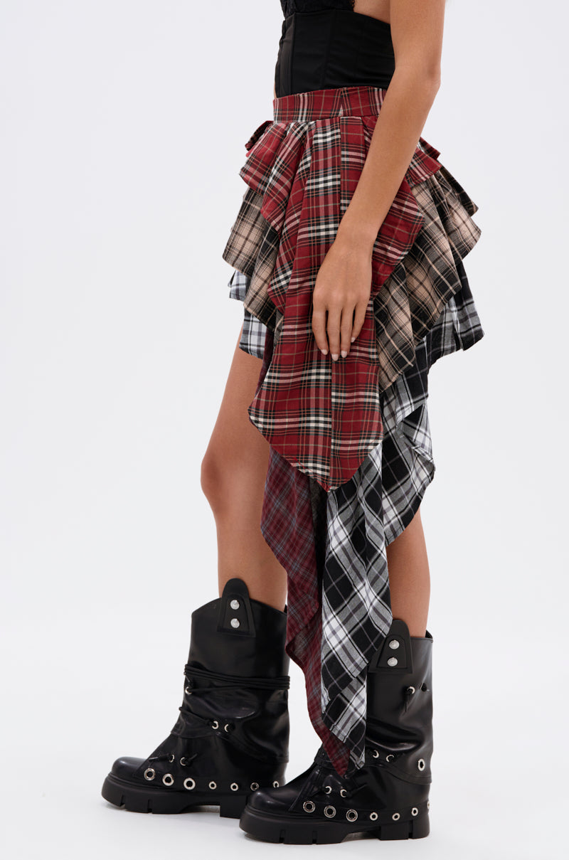 Wearing the SHAY MULTI PLAID MINI SKIRT in red, beige, and black with a black corset top and chunky knee-high boots, a person channels grunge style against a plain white background.